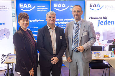 v.l. Ira Kummrow (Abteilungsleiter*in Kompetenzzentrum für Vermittlung und Integration), Steffen Leonhardi (Vorsitzender der Geschäftsführung der Agentur für Arbeit Leipzig), Tobias Schmidt (Hauptgeschäftsführer*in BBW-Leipzig-Gruppe) vor dem Stand der EAA Sachsen